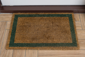 Brown natural rug with green contour in front of the white entrance door