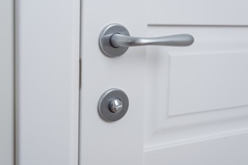 Detail of a white interior door with a chrome door handle and latch