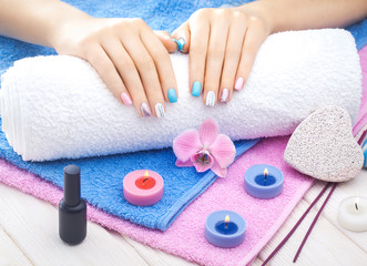 Obraz na płótnie Canvas beautiful colored manicure with orchid, candle and towel on the white wooden table.