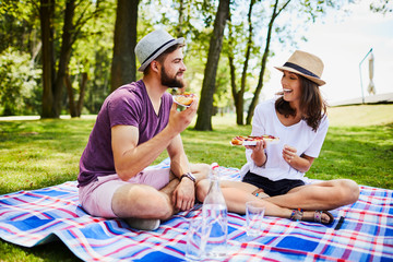 Cheerful young couple on a picnic outdoors eating together and laughing