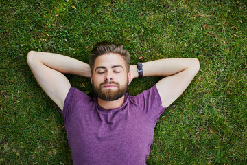 Young man lying on ground in park outdoors with eyes closed