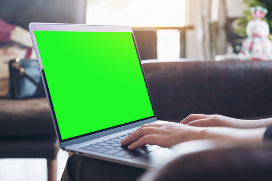 Mockup image of hands using and typing on laptop with blank green desktop screen in cafe