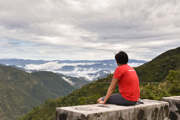 Naklejka na ściany i meble A man looking into the horizon while sitting on the ledge.
