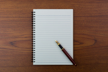 Fountain pen or ink pen with notebook paper on wooden working table with copy space, office desk concept. top view.