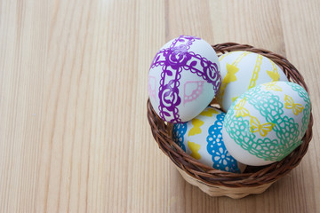 Easter eggs decorated in a wicker basket on a wooden background