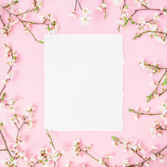Round frame with spring flowers and white paper vintage car on pink background. Flat lay, top view.