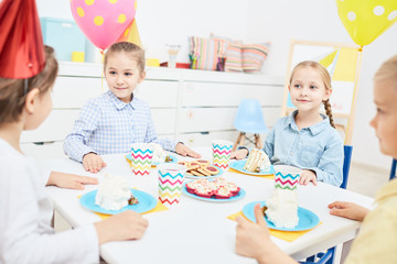 Group of friendly children gathered by festive table with desserts and drinks for birthday party