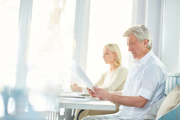 Obraz premium Mature serious financier reading documents while preparing for negotiation