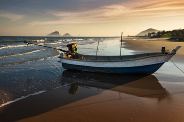 Sunset at the beach in Prachuab Khiri Khan, southen part of Thailand with the fishing boat on golden sand beach and colorful sky as a background.