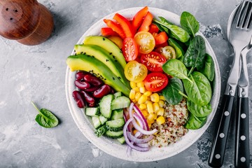 Healthy vegan lunch Buddha bowl. Avocado, quinoa, tomato, cucumber, red beans, spinach, red onion and red paprika vegetables salad.