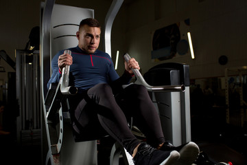 Fototapeta na wymiar Young sporty man sitting on training equipment and pulling handles while exercising