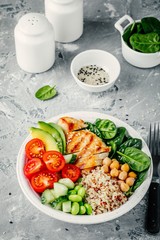 Buddha bowl with spinach salad, quinoa, chickpeas, grilled chicken, avocado, tomatoes, cucumbers, sesame seeds.