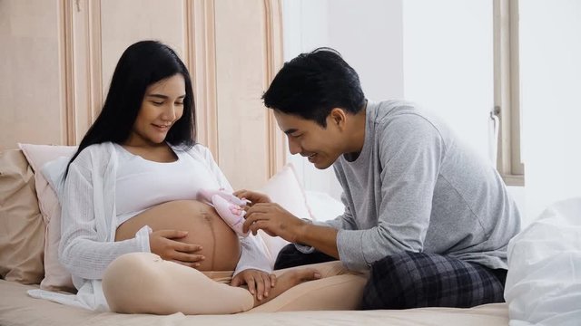 Young husband playing little shoes on belly pregnant wife