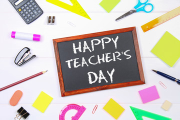 Text chalk on a chalkboard: Happy Teacher's Day. School supplies, office, books, apple.
