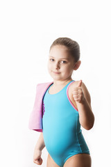 Little caucasian 7 years old cute caucasian girlie in cyan swimming costume shows thrumb up to camera