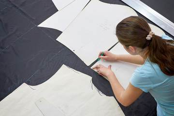 A cutter girl works at a large table with a marker marking the fabric for further sewing of work...