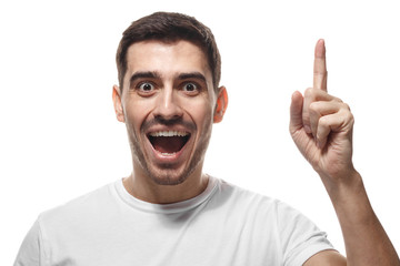 Close up portrait of young handsome smiling man in white t-shirt, pointing his finger in eureka sign, having great innovative idea, understanding solution