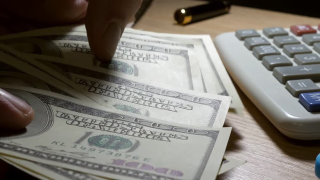 Man counting hungred dollar bills on a table with calculator.
