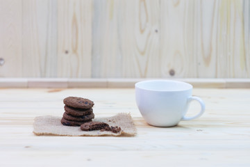 Chocolate chip cookies with a bite mark and a cup placed on a sack on a wooden table