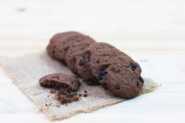 Chocolate chip cookies with a bite mark placed on a sack on a wooden table.