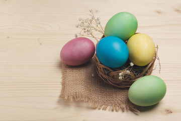 Colored eggs in a basket on a wooden surface. Easter still life