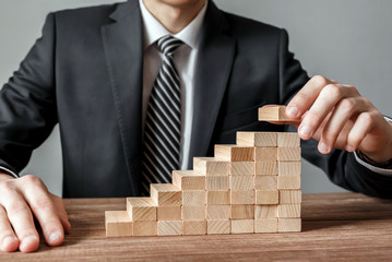 Businessman hand arranging stacking wooden blocks development as step stair. Business growth...