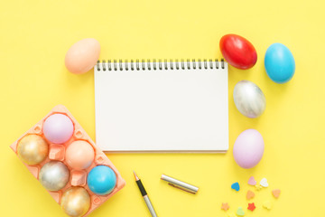 Flat lay top view colorful easter egg painted in pastel colors composition and mock up blank notebook with paint brush on yellow pastel color background. Easter day background top view with copy space