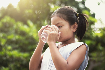 Fototapeta premium asian little girl drinking water from glass with sunshine background