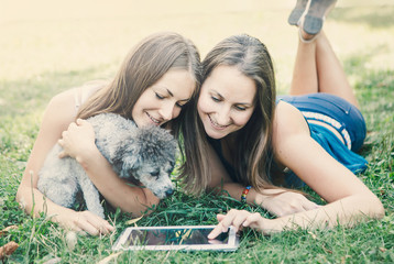 Happy young women hugging dog and looking in laptop. Relaxing in the park.