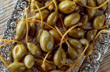 Pickled caper berries in metal dish .