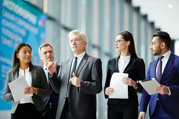 Aged politician in suit talking to his team while walking to conference hall