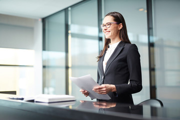 Young businesswoman or delegate with papers making report at conference or political summit