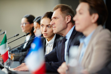 One of young speakers consulting with mature delegate while listening to other participants of...