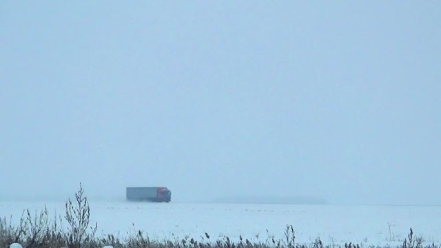 A truck with red cabin and a large van quickly goes on snow-covered road left to right