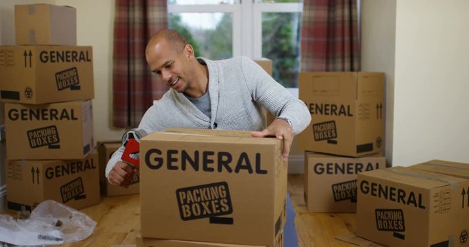 4K Portrait happy mixed race man packing boxes in new home & smiling to camera. Slow motion.