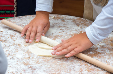 Child hands rolling dough with rolling pin on wooden table