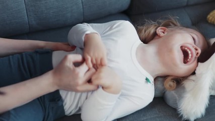 Happy mother having fun with her kid daughter tickling on sofa home woman baby hand love child girl face young cheerful little beautiful happy joy smile childhood cute together laugh lying activities