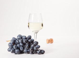 Two glasses and a bottle of white wine, on a white background near a handful of grapes