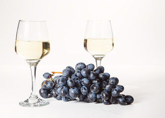 Two glasses and a bottle of white wine, on a white background near a handful of grapes