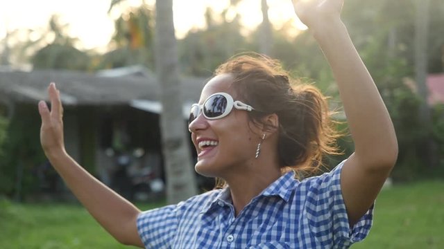Happy stylish young woman in sunglasses dancing in the sun sings song between tropical palm trees in jungle. Slow Motion. 1920x1080