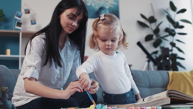 Smiling mother with little daughter painting paper together smiling kid family hobby baby design love person girl house coloring mom play art paintbrush childhood happy home table artist closeup talk