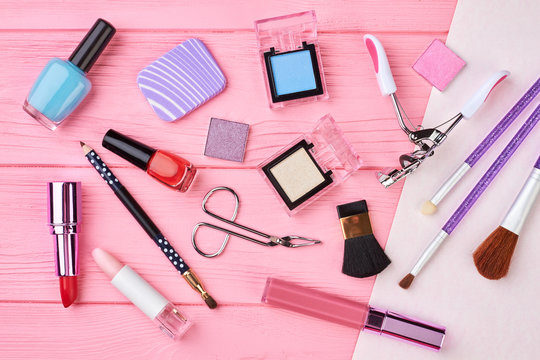 Flat lay female cosmetics essentials, top view. Cosmetics and beauty equipment on pink wooden background. Beauty makeup products.