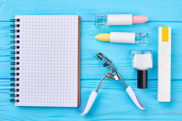 Cosmetics and paper notebook. Flat lay of decorative cosmetics, eyelashes curler and blank paper notepad.