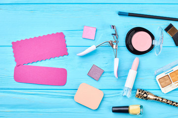 Colorful cosmetics set on blue background. Decorative cosmetics essentials and tools for make up. Pink paper card for text. Beauty and fashion concept.