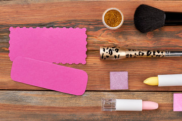 Fototapeta na wymiar Makeup cosmetics on wooden background. Cosmetics products and tools. Pink blank card for text. Beauty and fashion concept.