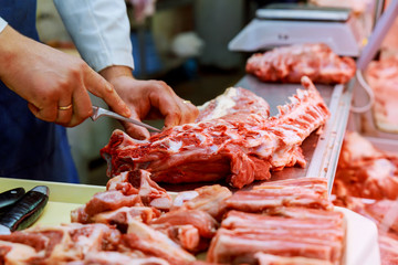 Cropped image of male butcher cutting raw meat with knife at counter shop