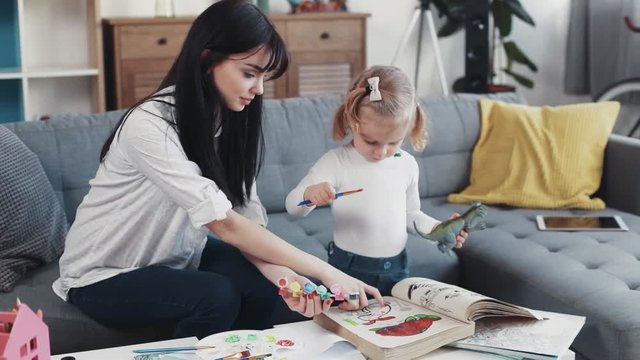 mom sitting with baby holding dinosaur toy hugging draw together on sofa at home talking kid family hobby love girl house coloring mom play art paintbrush childhood happy home table artist closeup