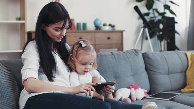 Child with mother sit on sofa use phone look some interesting hug woman baby hand love child girl kid internet cartoon technology smartphone face home mobile touch mom game little play application