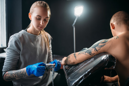 Tattooist makes tattoo by machine on male shoulder
