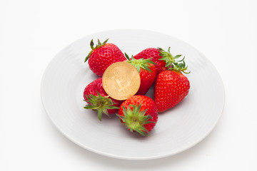 Strawberries and cryptocurrency arranged on plate isolated 